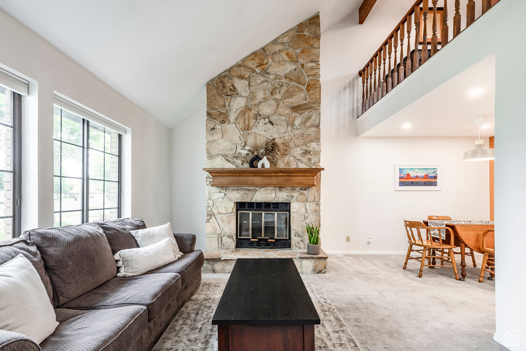 Carpeted living area featuring high vaulted ceiling, a stone fireplace, and baseboards