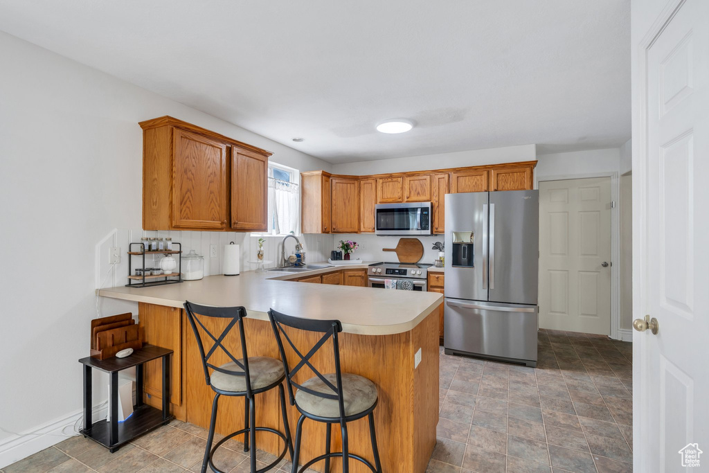 Kitchen with stainless steel appliances, a peninsula, brown cabinets, light countertops, and a sink