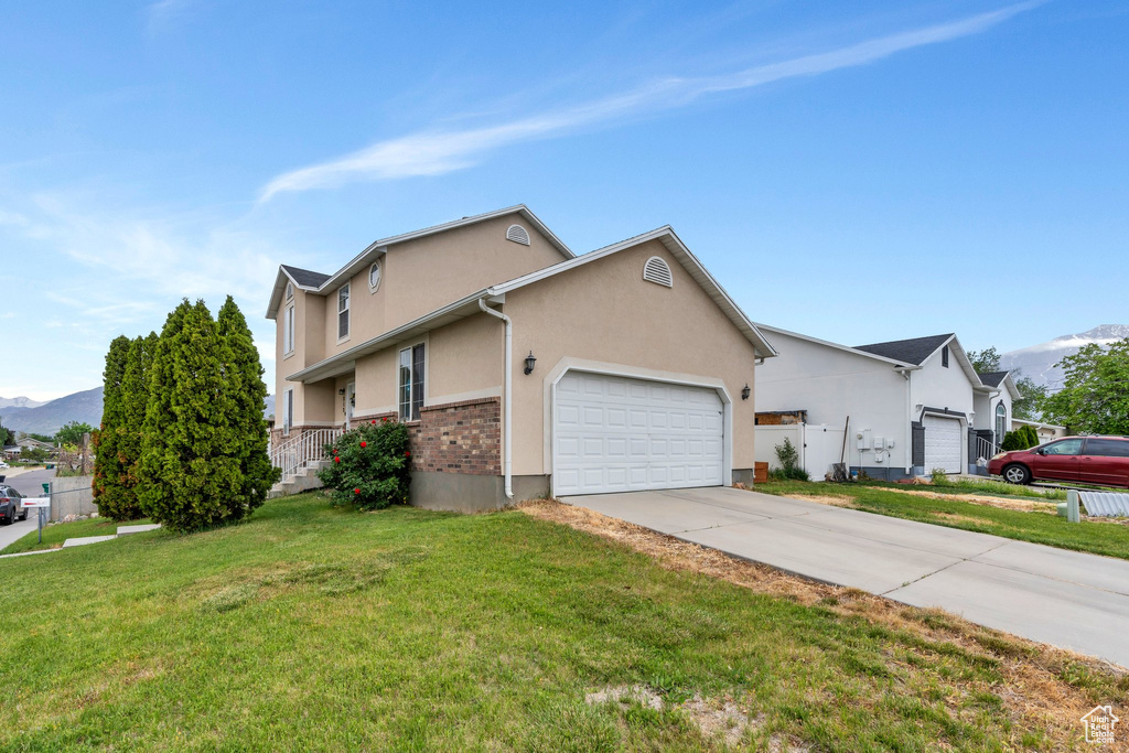View of front of property featuring a garage, a front yard, driveway, stucco siding, and a mountain view