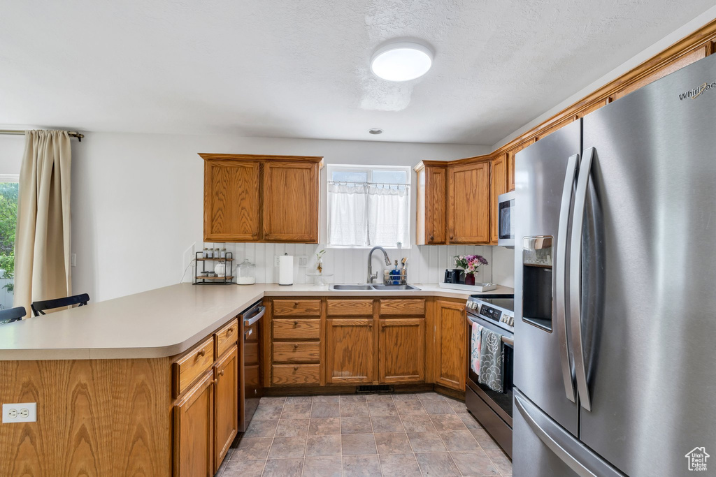 Kitchen featuring stainless steel appliances, a peninsula, a sink, light countertops, and brown cabinets