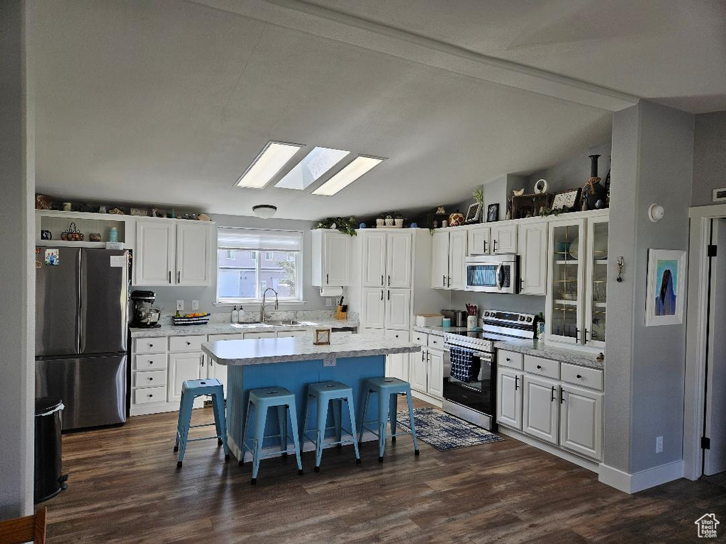 Kitchen with stainless steel appliances, a breakfast bar, white cabinetry, a skylight, and lofted ceiling