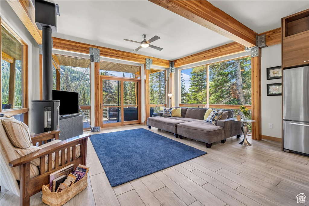Living area featuring beam ceiling, ceiling fan, a wood stove, and light wood-style floors