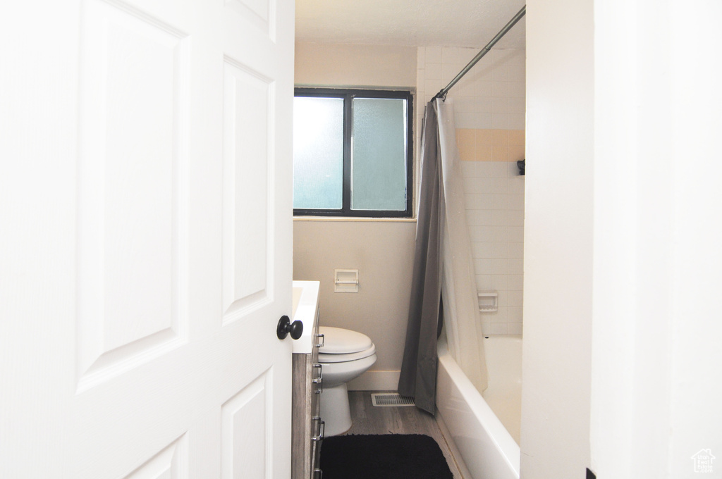 Full bathroom featuring toilet, shower / bath combo with shower curtain, wood finished floors, vanity, and baseboards
