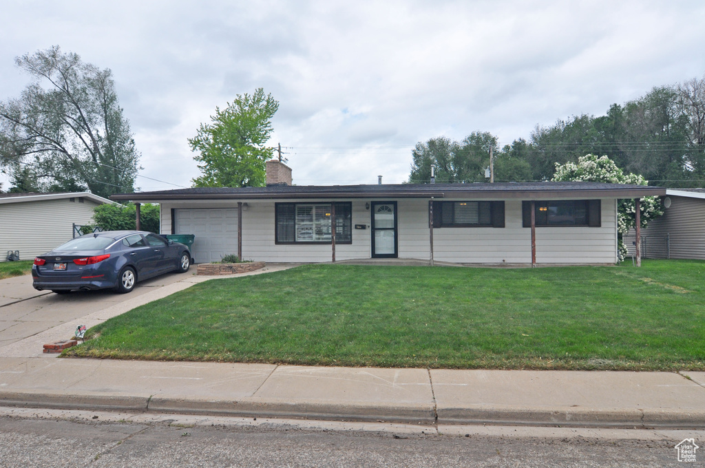 Single story home featuring an attached garage, concrete driveway, a front yard, and a chimney