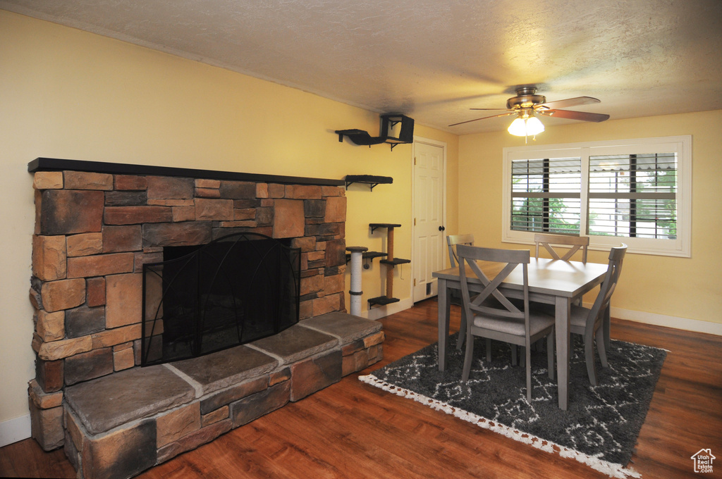 Dining space featuring ceiling fan, wood finished floors, a fireplace, baseboards, and a textured ceiling