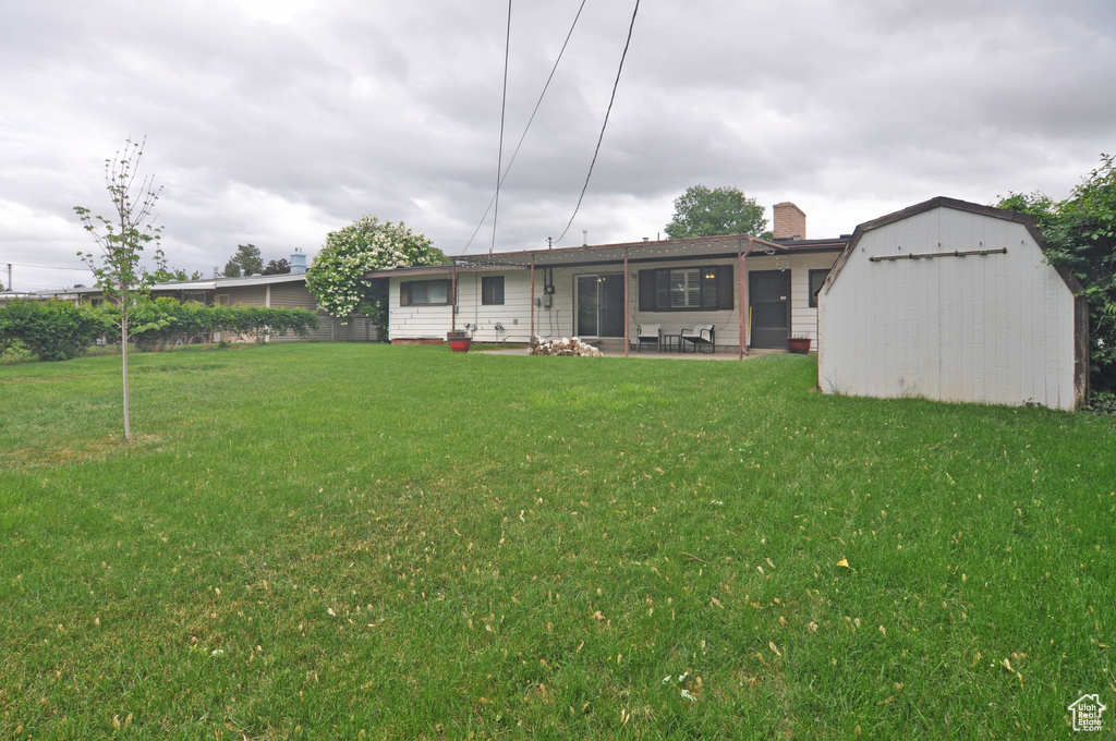 Rear view of house featuring a lawn, a garage, a patio, and an outbuilding