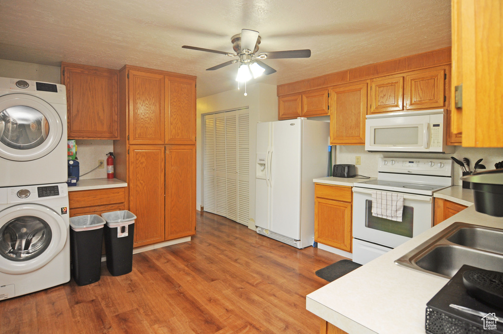 Kitchen with white appliances, stacked washer / dryer, light countertops, and light wood-style flooring