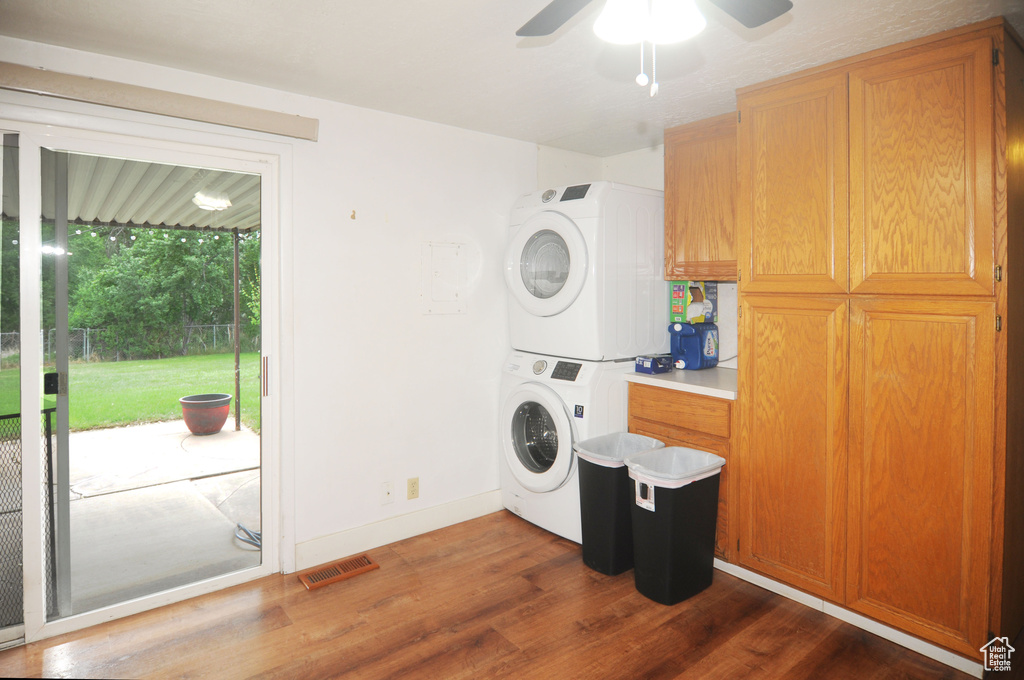 Clothes washing area featuring stacked washing machine and dryer, dark wood-style flooring, a ceiling fan, and baseboards