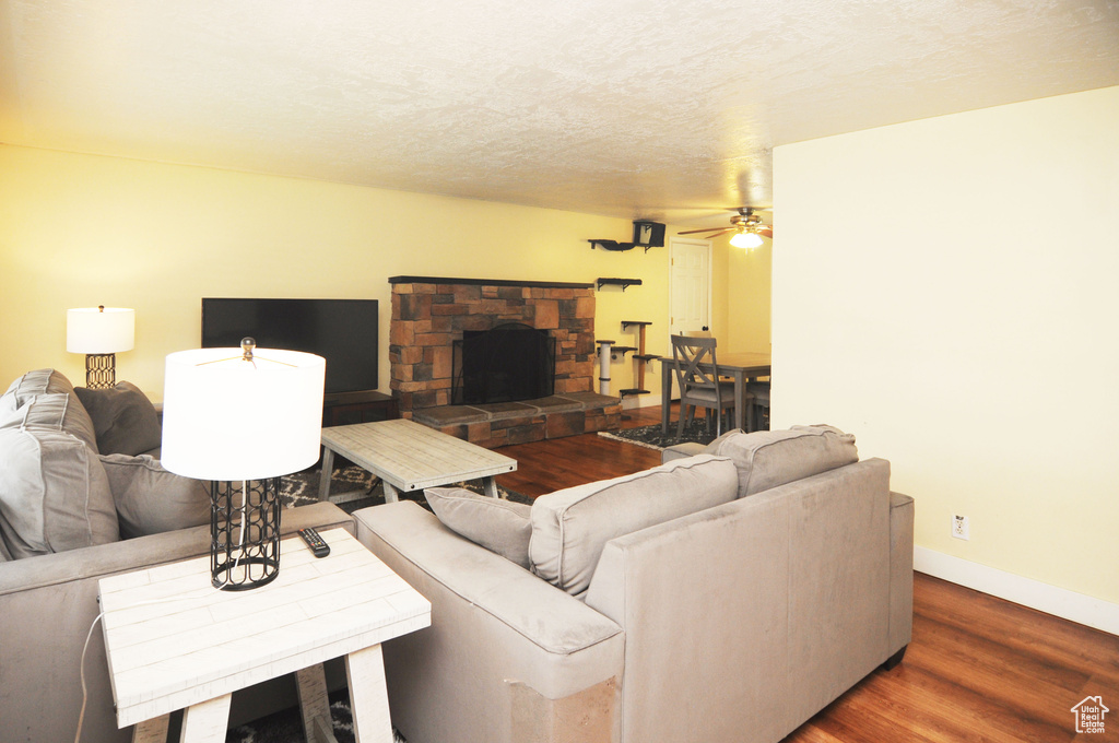 Living area with ceiling fan, wood finished floors, baseboards, and a stone fireplace