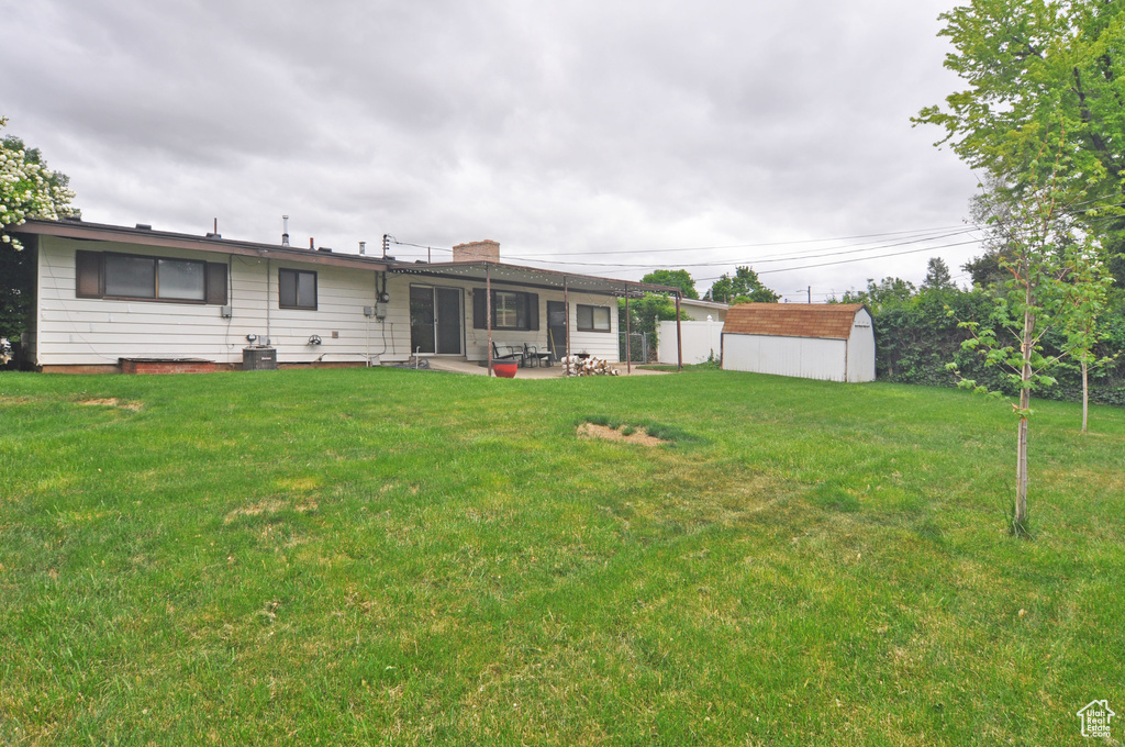 Back of house with a patio, a storage unit, an outbuilding, a lawn, and a chimney