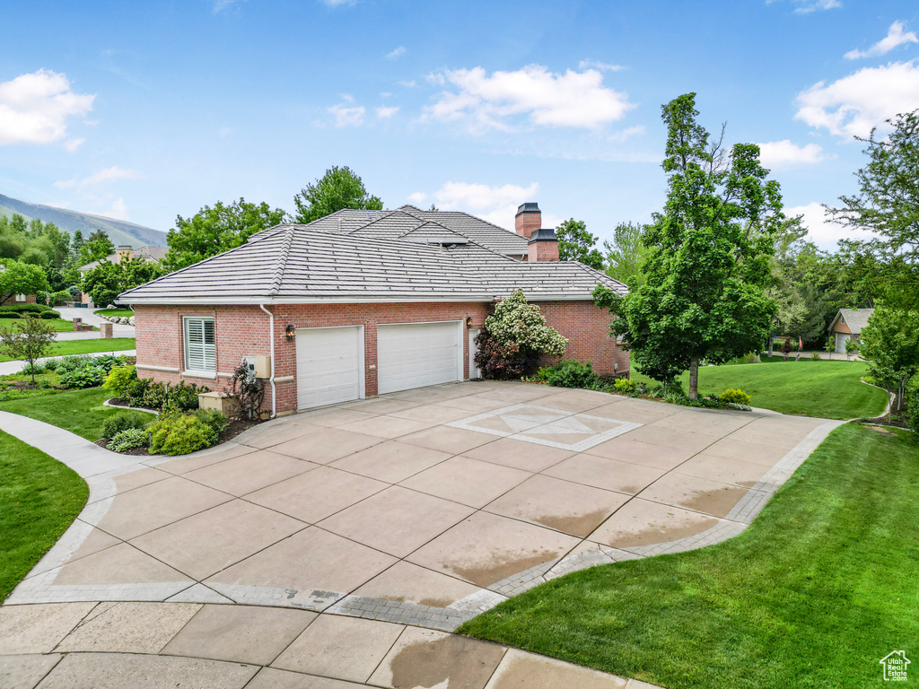 View of side of property featuring a yard, a garage, concrete driveway, brick siding, and a tiled roof