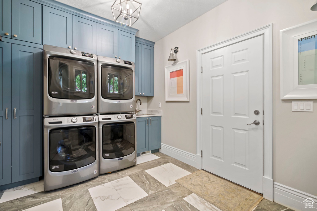 Laundry area featuring cabinet space, stacked washer / dryer, baseboards, light marble finish flooring, and a chandelier