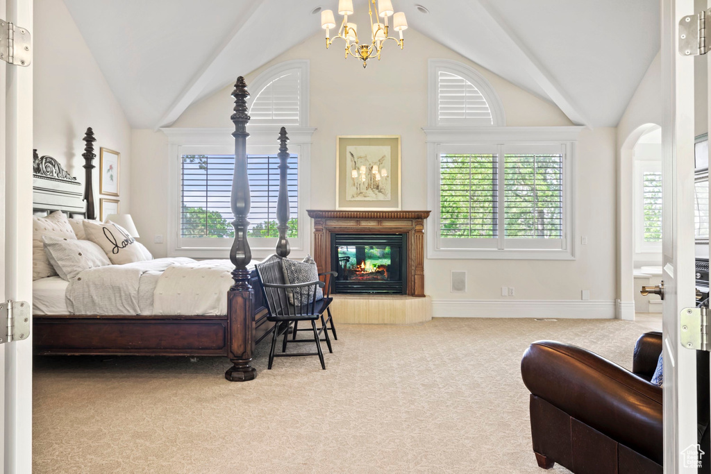 Carpeted bedroom with a chandelier, lofted ceiling, a glass covered fireplace, and baseboards
