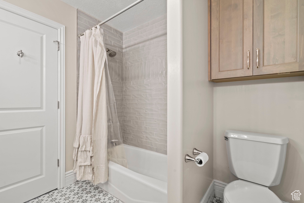Full bathroom with tile patterned floors, toilet, shower / tub combo with curtain, and baseboards