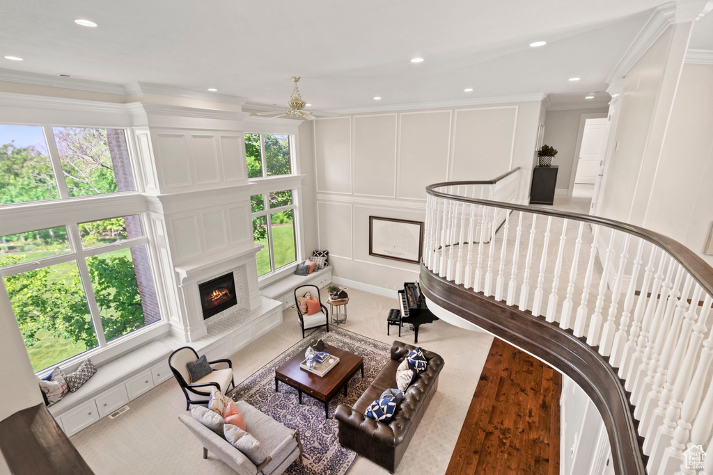 Carpeted living room with a decorative wall, crown molding, a fireplace, ceiling fan, and recessed lighting