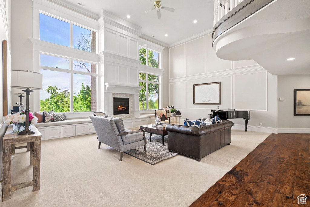 Living area featuring a towering ceiling, a decorative wall, a fireplace, crown molding, and ceiling fan