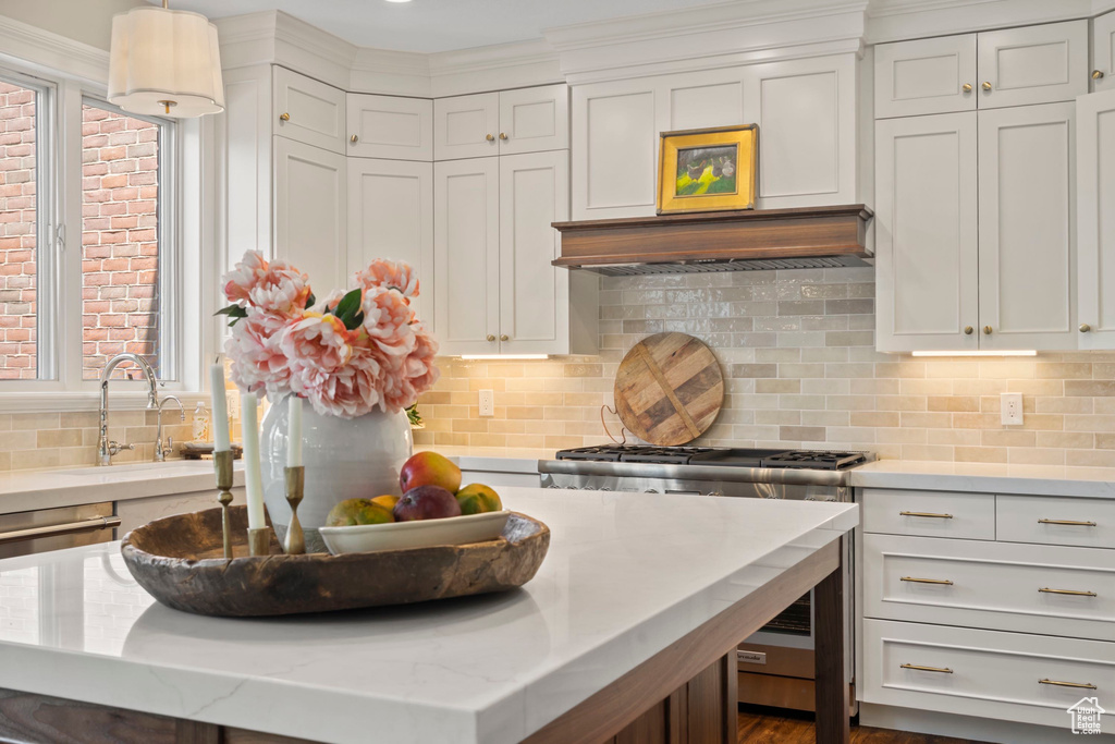 Kitchen with gas stove, a sink, decorative backsplash, white cabinetry, and hanging light fixtures