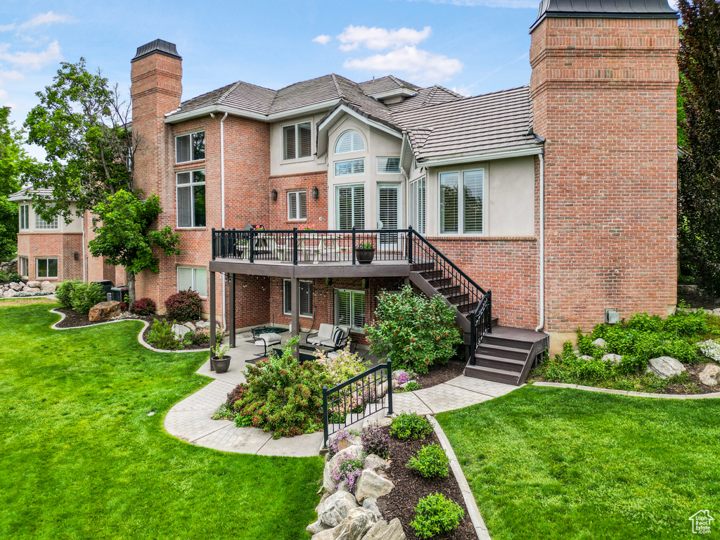 Back of property with a chimney, a deck, a patio, brick siding, and stairway