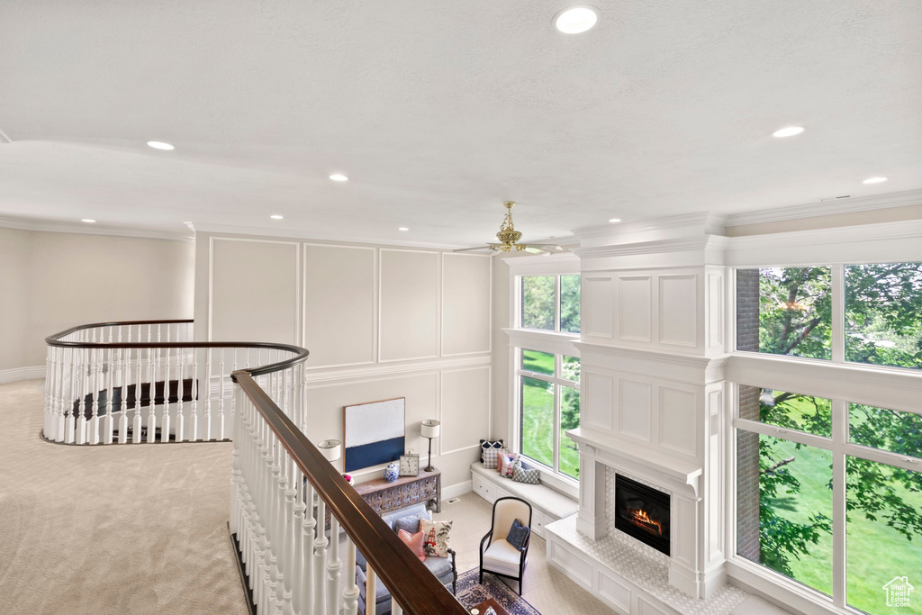 Corridor with an upstairs landing, light carpet, a decorative wall, ornamental molding, and recessed lighting