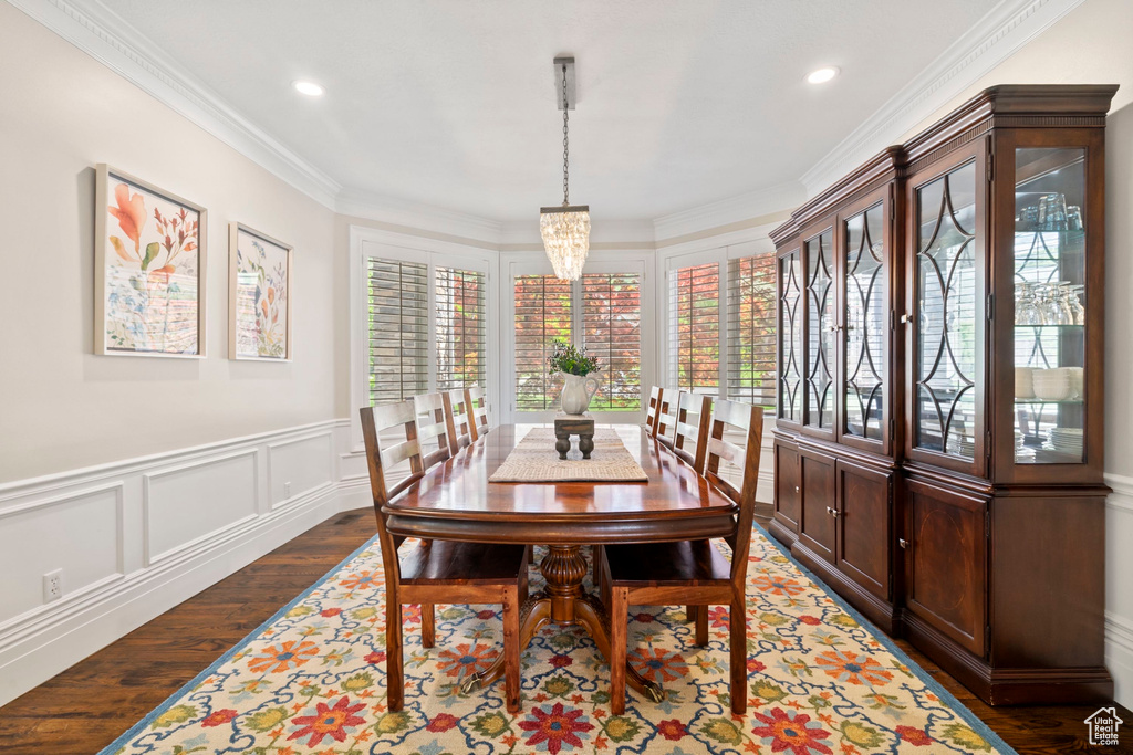 Dining space with dark wood-style floors, ornamental molding, a chandelier, recessed lighting, and a wainscoted wall