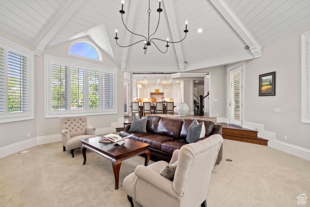 Living room with a chandelier, beam ceiling, light colored carpet, plenty of natural light, and high vaulted ceiling