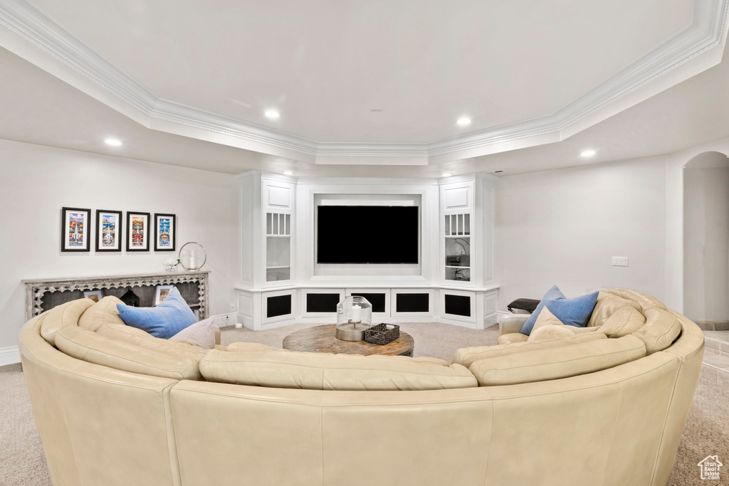 Carpeted living room featuring recessed lighting, crown molding, a raised ceiling, baseboards, and arched walkways