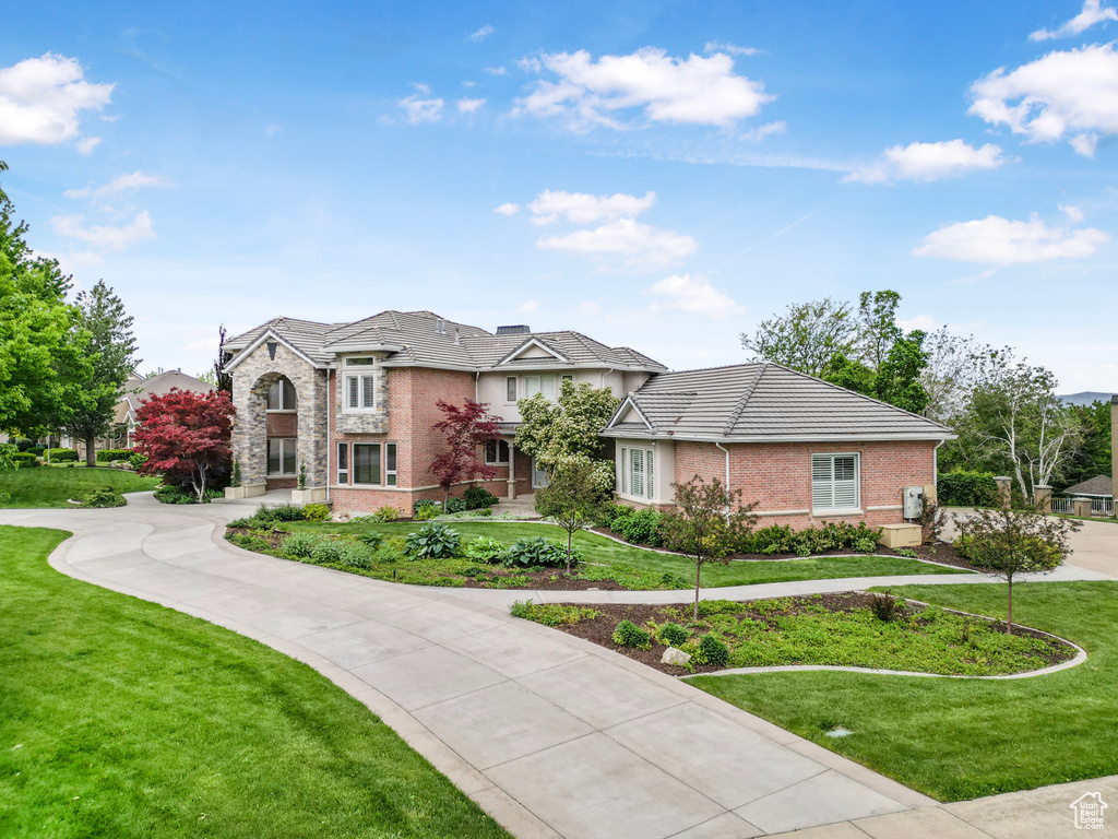 View of front of house with a front lawn, stone siding, curved driveway, and a tiled roof