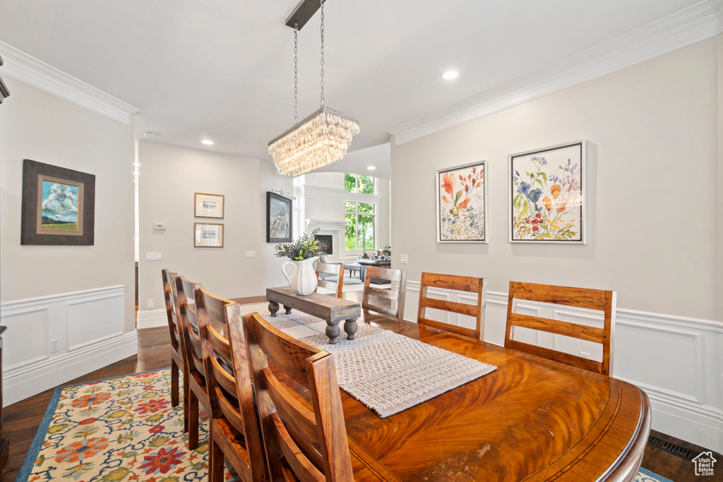 Dining area with crown molding, dark wood-style flooring, a wainscoted wall, recessed lighting, and a chandelier