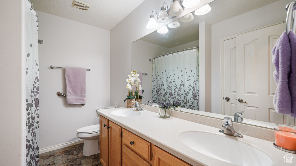 Bathroom with baseboards, toilet, double vanity, and stone finish floors