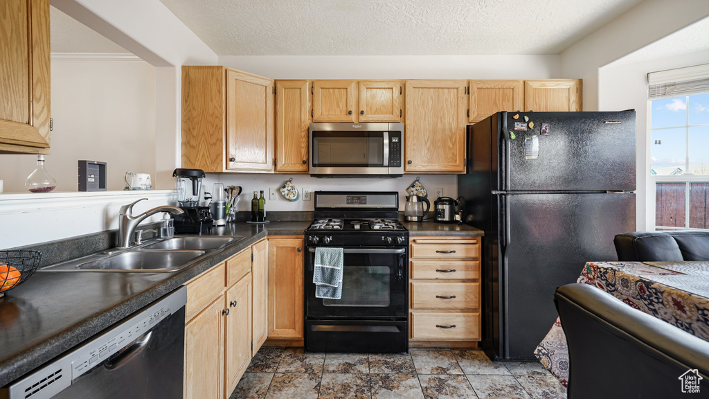 Kitchen featuring black appliances, dark countertops, a sink, light brown cabinetry, and light stone finish floors