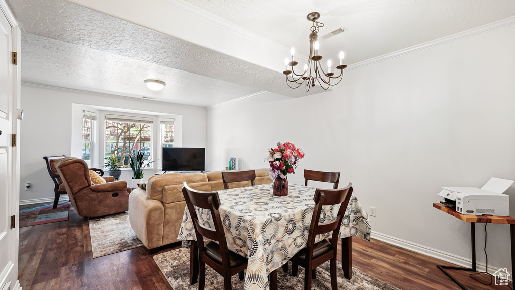 Dining room featuring dark wood-style floors, a chandelier, crown molding, baseboards, and a textured ceiling