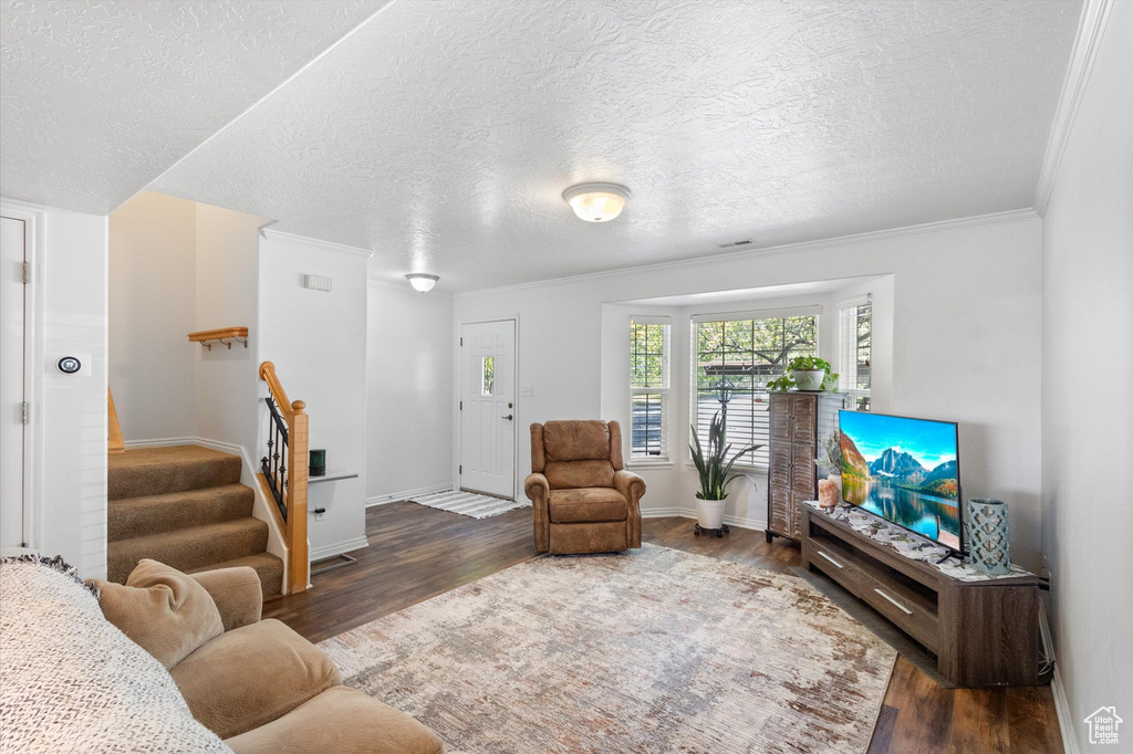Living area with wood finished floors, stairs, a textured ceiling, and ornamental molding