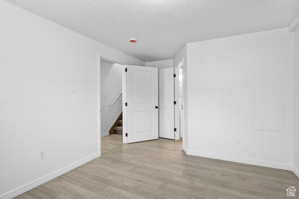 Empty room featuring light wood-type flooring, baseboards, and a textured ceiling