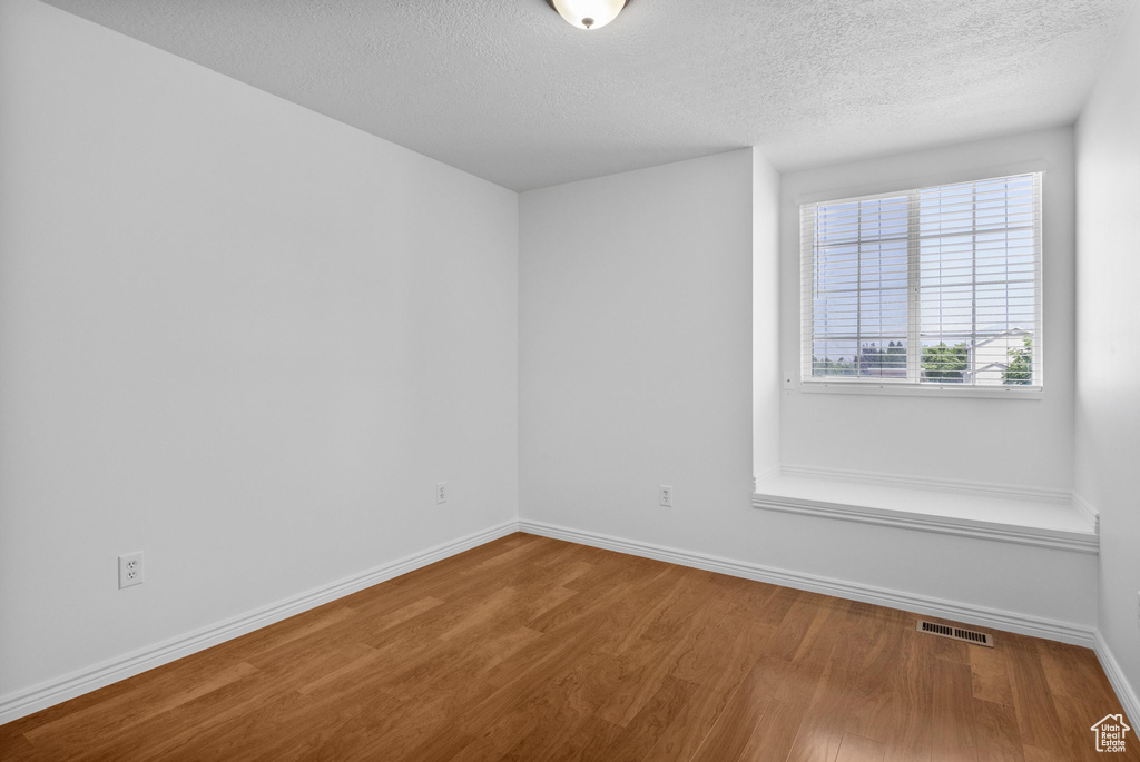 Unfurnished room with wood finished floors, a textured ceiling, and baseboards