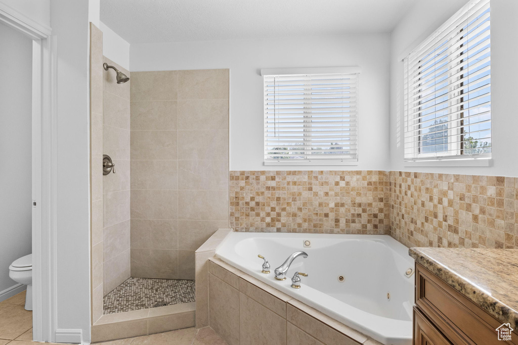 Full bath with a jetted tub, tiled shower, toilet, vanity, and tile patterned flooring