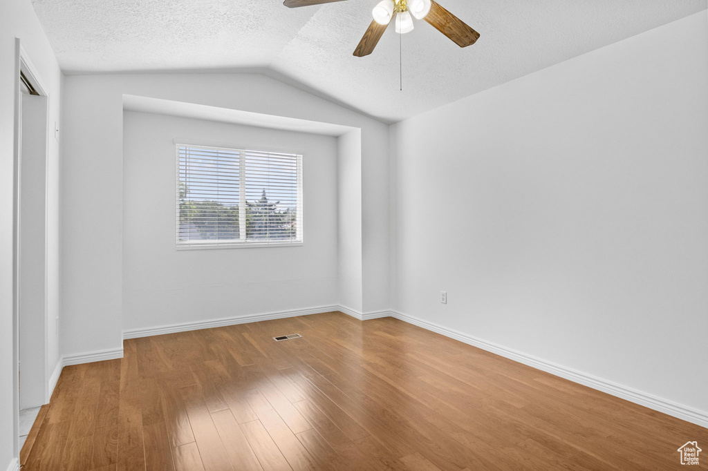Empty room with a ceiling fan, wood finished floors, vaulted ceiling, a textured ceiling, and baseboards