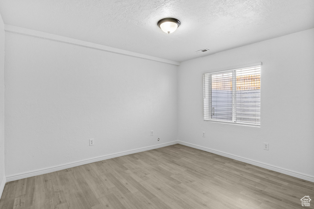 Empty room with light wood-style floors, a textured ceiling, and baseboards