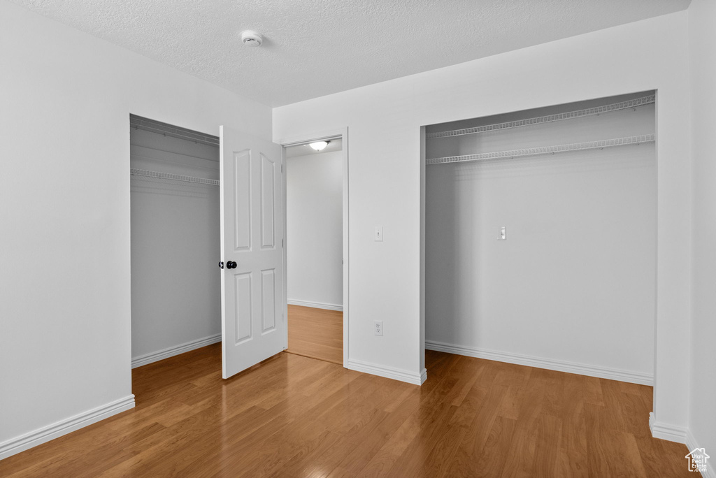 Unfurnished bedroom featuring wood finished floors, baseboards, a textured ceiling, and multiple closets