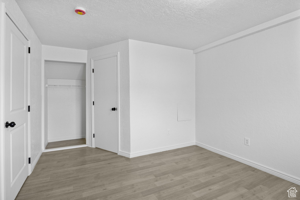 Unfurnished bedroom featuring a textured ceiling, wood finished floors, baseboards, and a closet