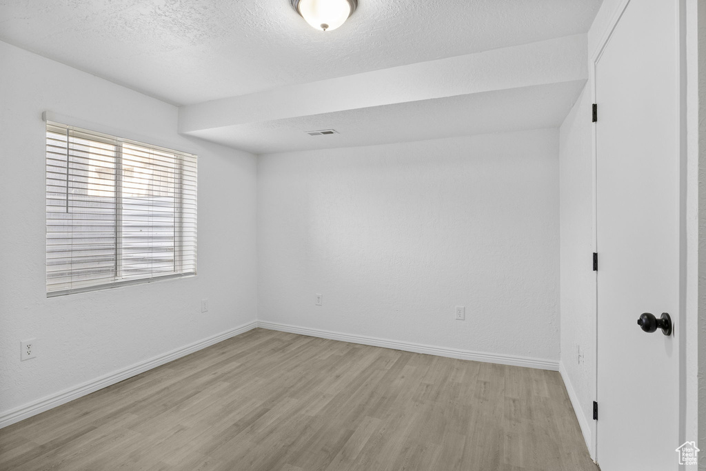 Empty room featuring light wood-type flooring, baseboards, and a textured ceiling