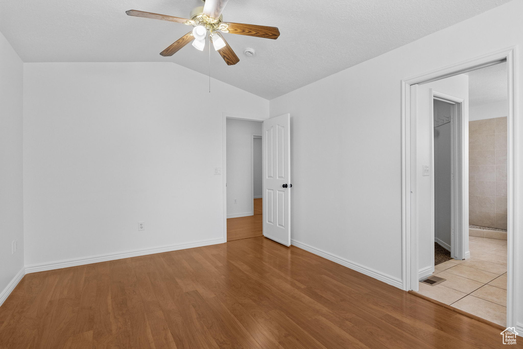 Unfurnished bedroom with vaulted ceiling, wood finished floors, baseboards, ceiling fan, and a walk in closet