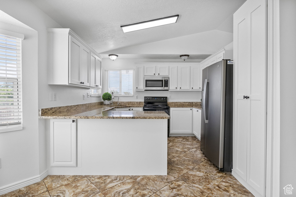 Kitchen featuring stainless steel appliances, lofted ceiling, a peninsula, white cabinetry, and light stone counters