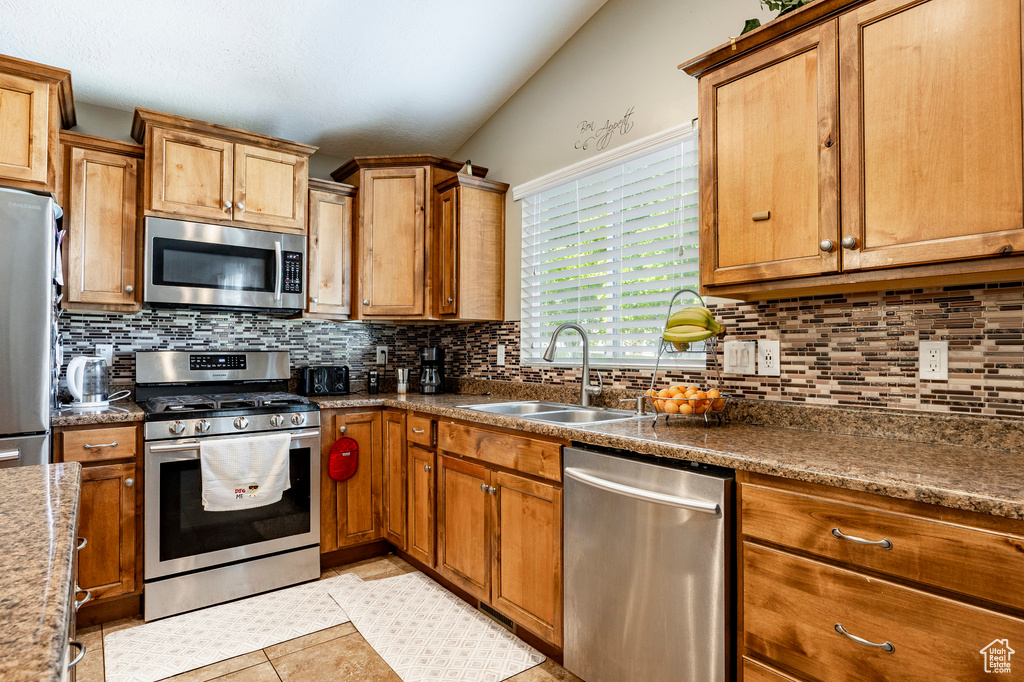 Kitchen featuring light tile patterned floors, a sink, brown cabinets, tasteful backsplash, and appliances with stainless steel finishes