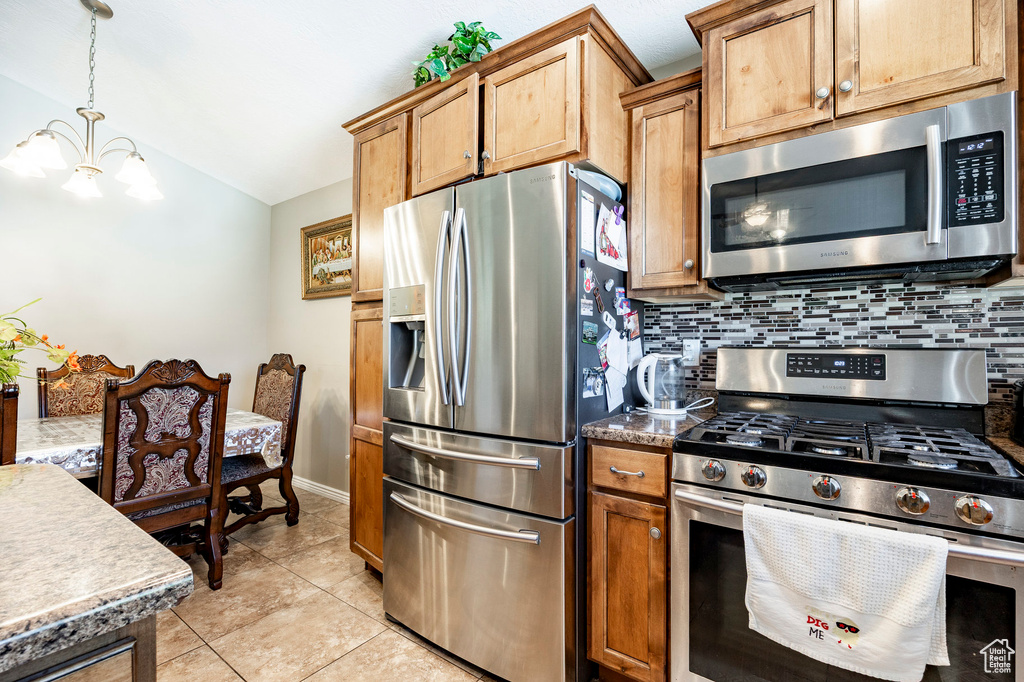 Kitchen featuring tasteful backsplash, vaulted ceiling, an inviting chandelier, light tile patterned floors, and appliances with stainless steel finishes