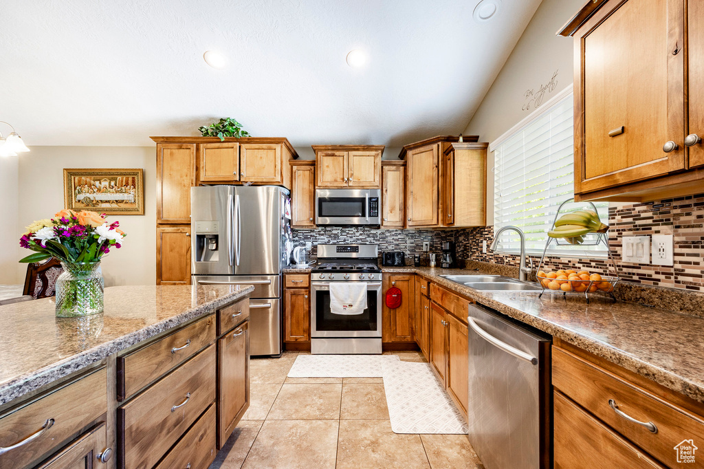 Kitchen with appliances with stainless steel finishes, brown cabinetry, tasteful backsplash, and a sink
