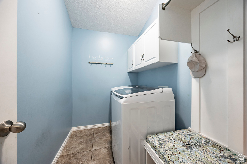 Clothes washing area with washing machine and clothes dryer, a textured ceiling, cabinet space, and baseboards