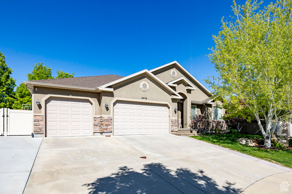 View of front of house featuring fence, an attached garage, stone siding, concrete driveway, and stucco siding