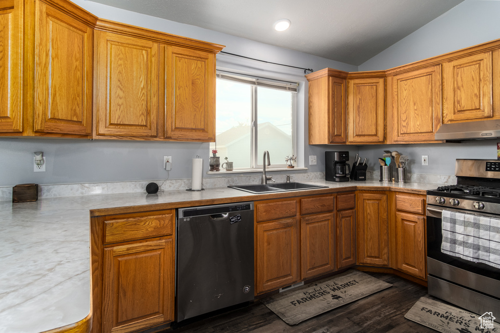 Kitchen with appliances with stainless steel finishes, a sink, under cabinet range hood, light countertops, and lofted ceiling