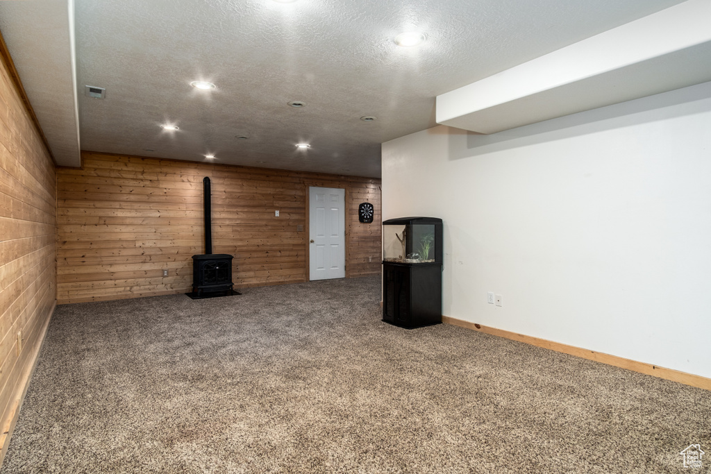 Finished basement with a wood stove, carpet, a textured ceiling, wooden walls, and recessed lighting