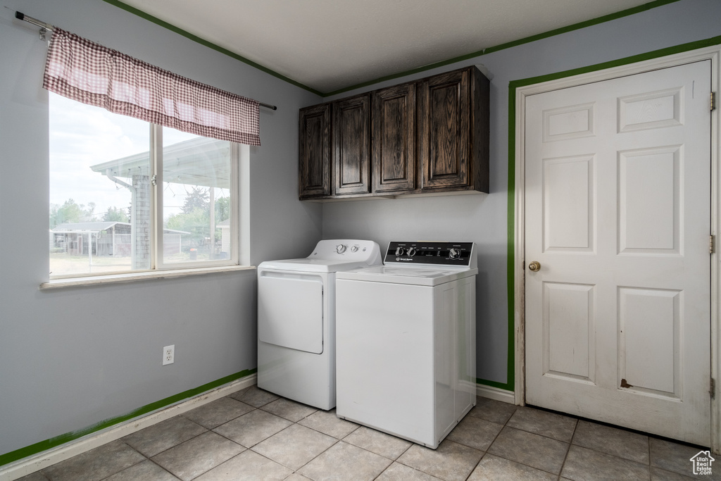 Clothes washing area with washer and clothes dryer, cabinet space, baseboards, and light tile patterned floors